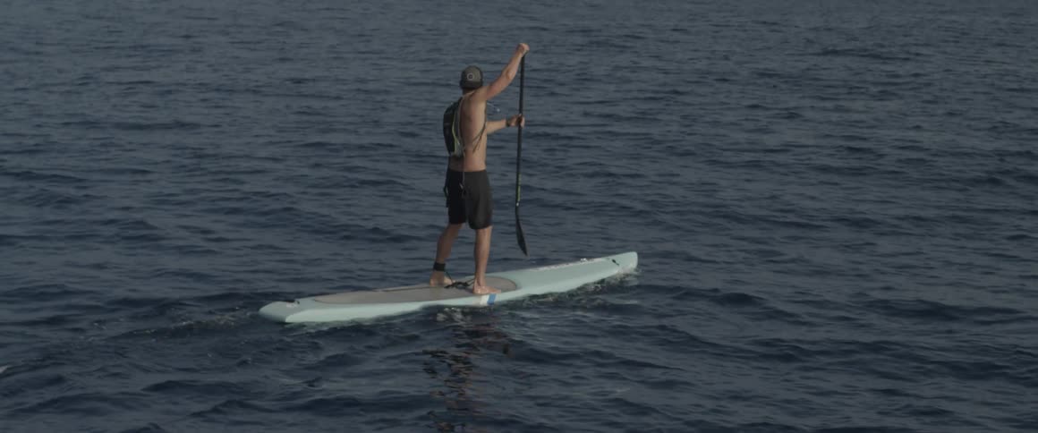 A man is paddling on his surfboard with an oar