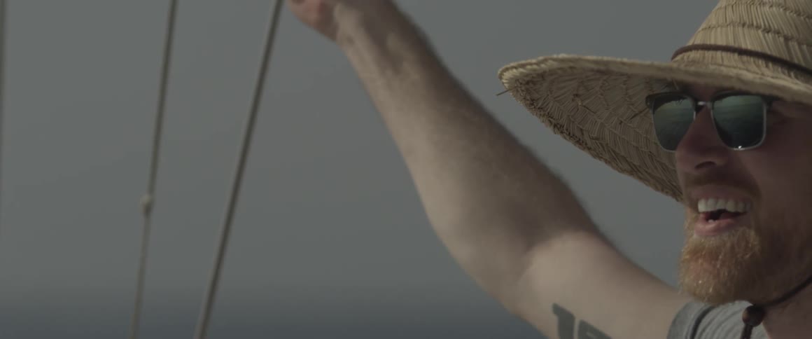 A man in a straw hat rides on a sailboat