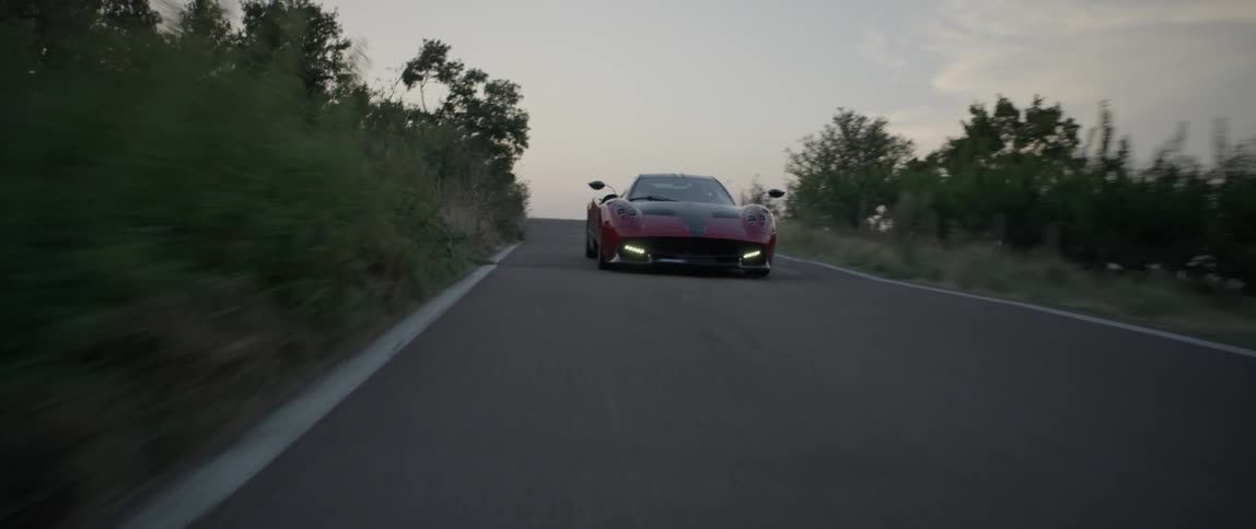 A red sports car drives at sunset around winding turns