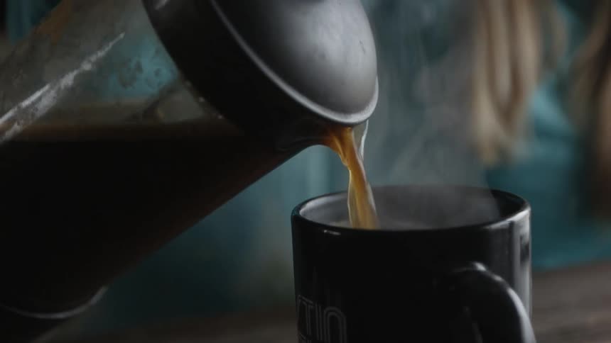 Coffee is being poured from a french press into a mug