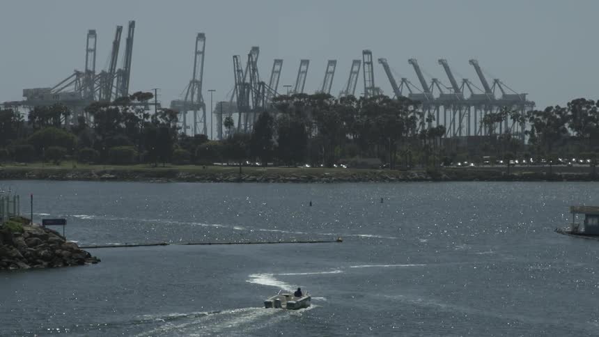 A boat travels in a harbor near an shipping port