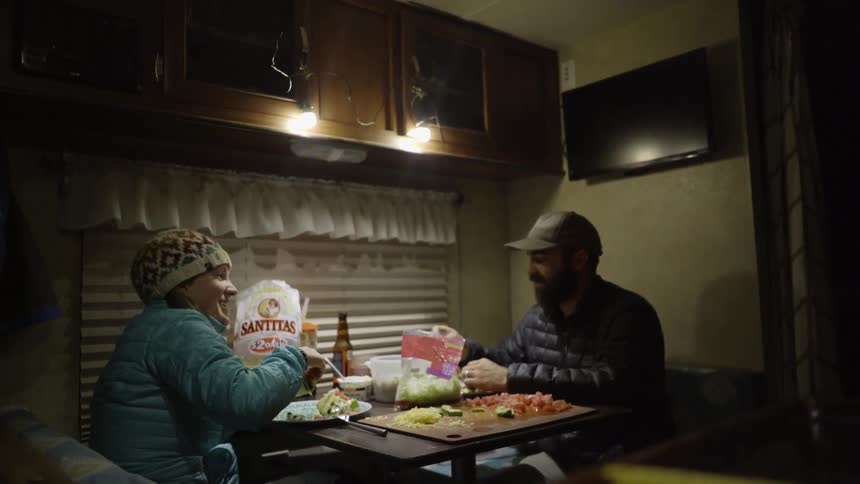 A man and woman eat at a camper table