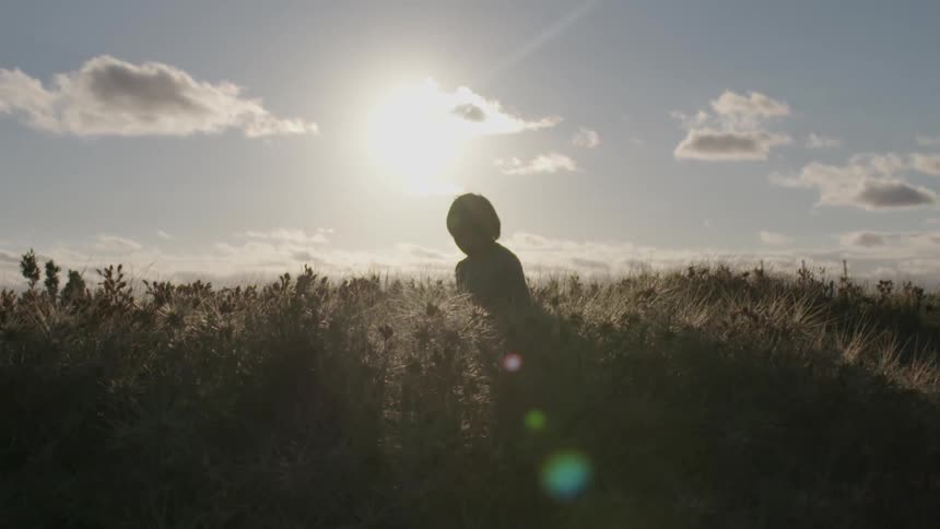 A young boy stands in a tall grass field