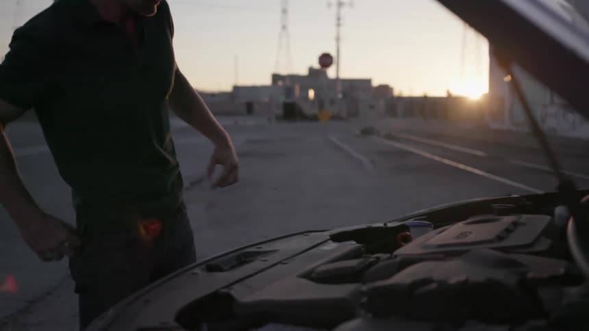 A man lifts the hood of a car and steam rises
