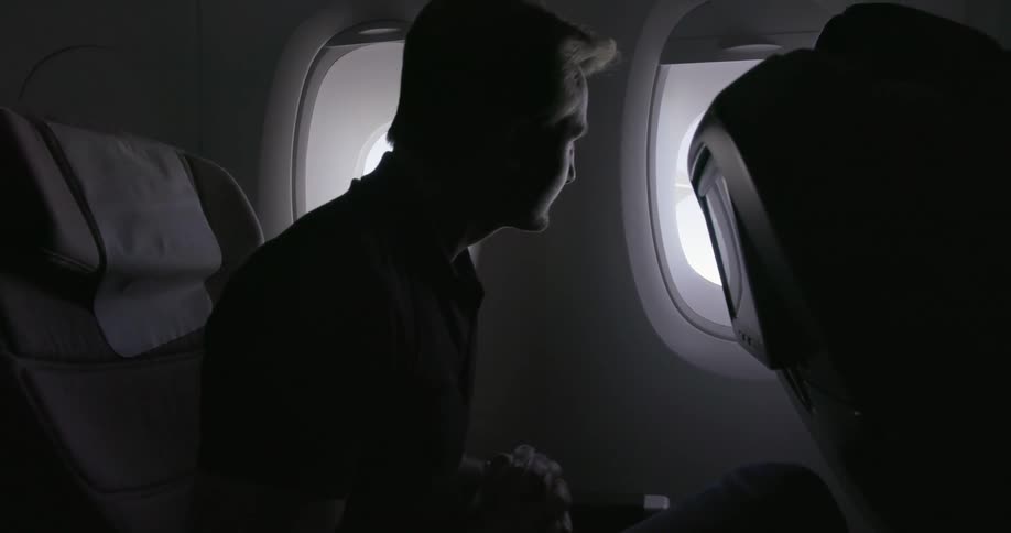 A man sits up to look out the plane window then leans back
