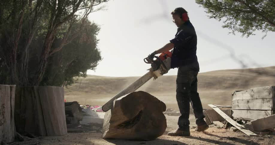 A man uses a chainsaw to cut a large piece of wood