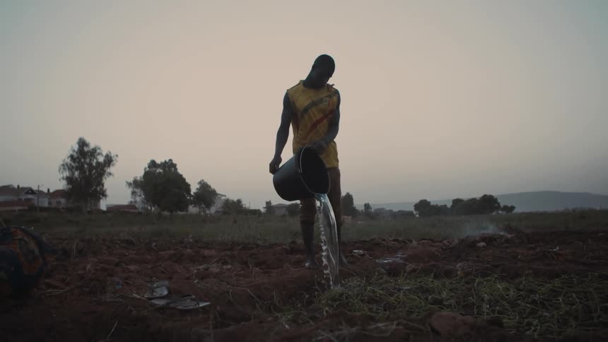 A man pours a bucket of water in a dirt field