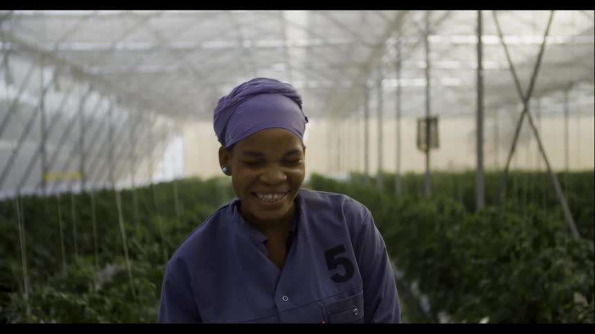 A woman smiles and laughs while standing in a greenhouse
