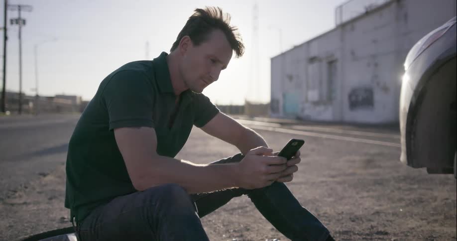A man uses his phone while sitting on a tire