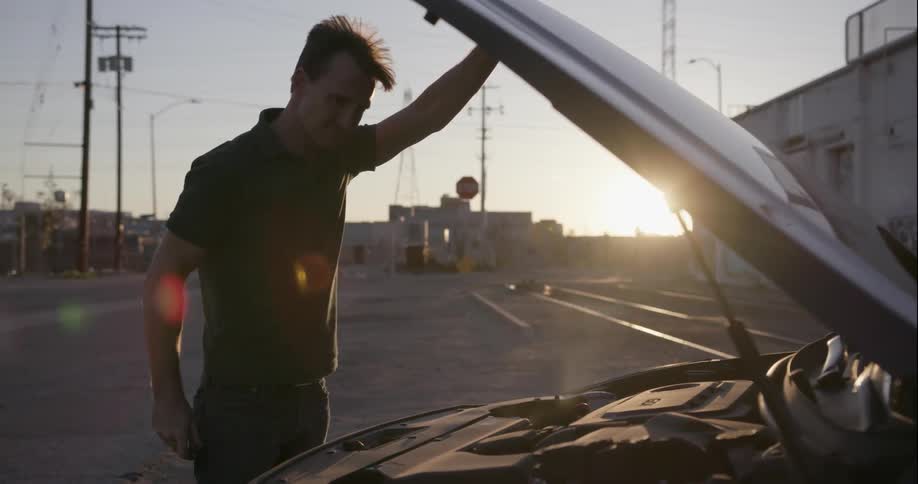A man opens the hood of his car to check why it is smoking