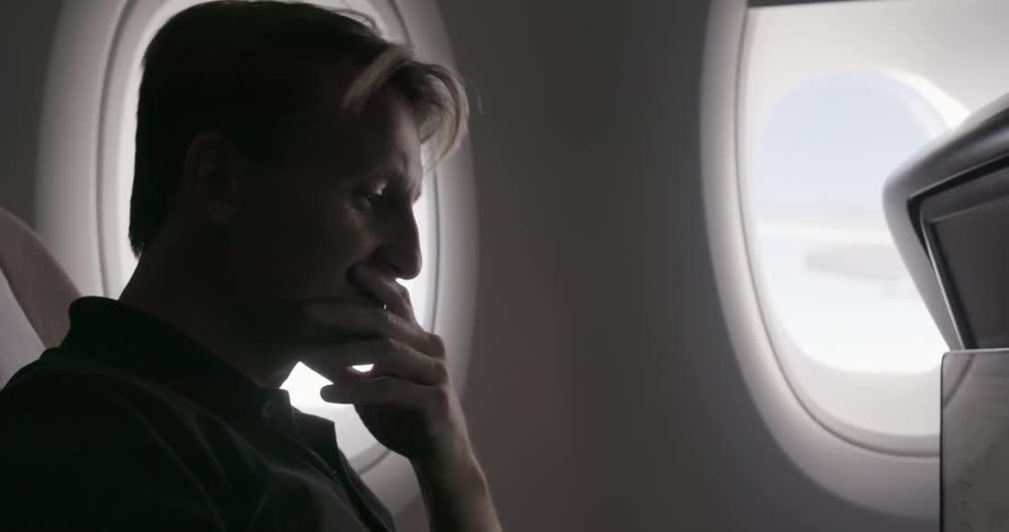 A man is looking at his computer during a flight
