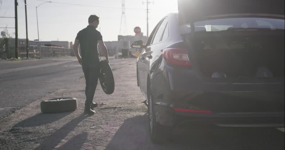 A pulls a spare tire from the trunk of a car