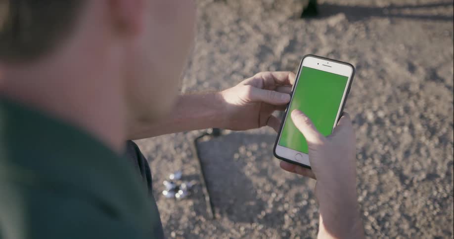 Man outside next to lug nuts and tire iron holding cell phone with green screen