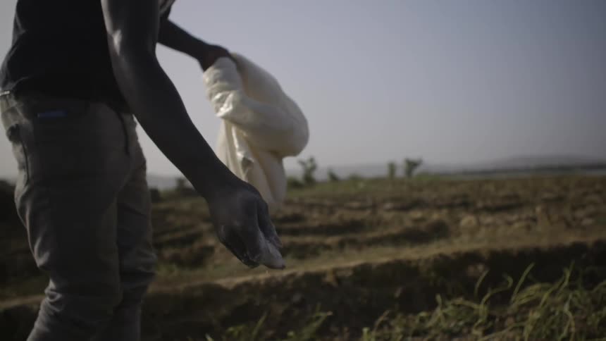A man throws fertilizer onto a rural field