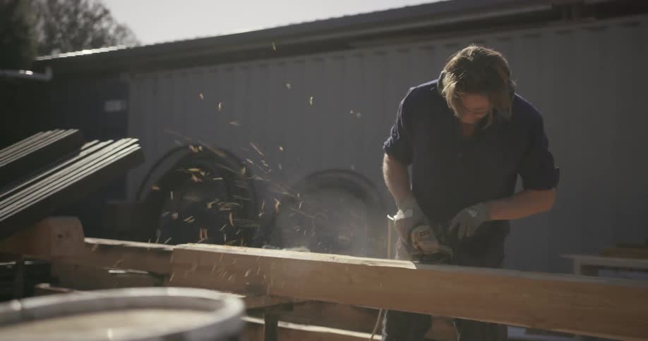 Man sanding large piece of wood with electric sander outside during the day