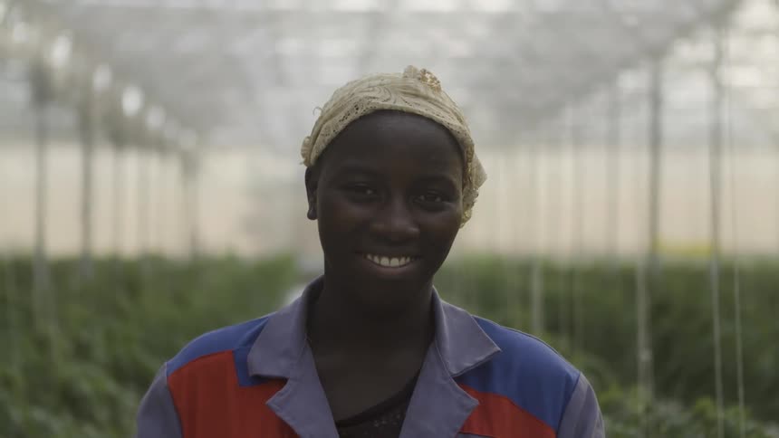 An african woman is smiling as she stands in a greenhouse