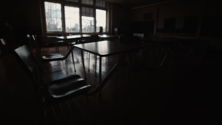 Desks sit in shadow in an empty school classroom