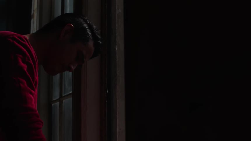 A man is leaning by a window in a dark room