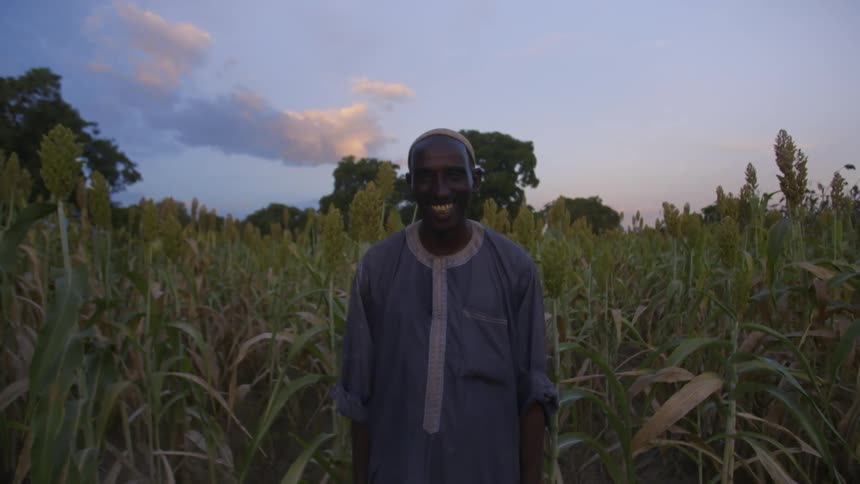 An african man smiles as he stands in a corn field