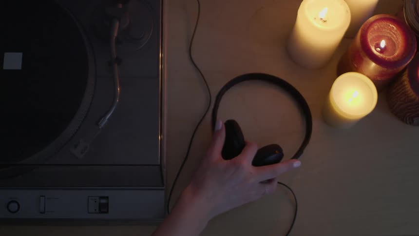 A person picks up their headphones by the record player
