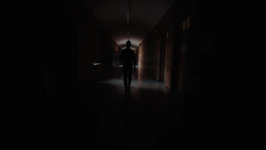 A man is walking down a dark hallway in a building