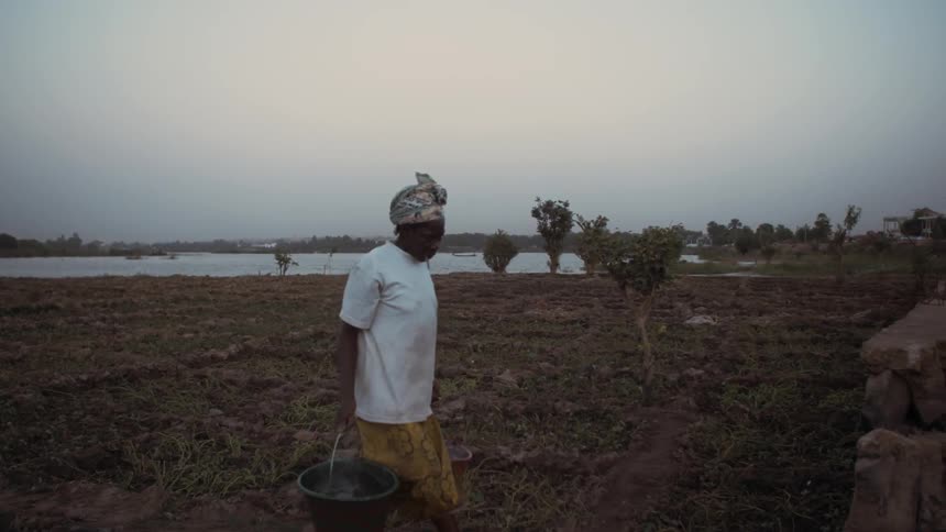 A woman carries full water buckets to a garden