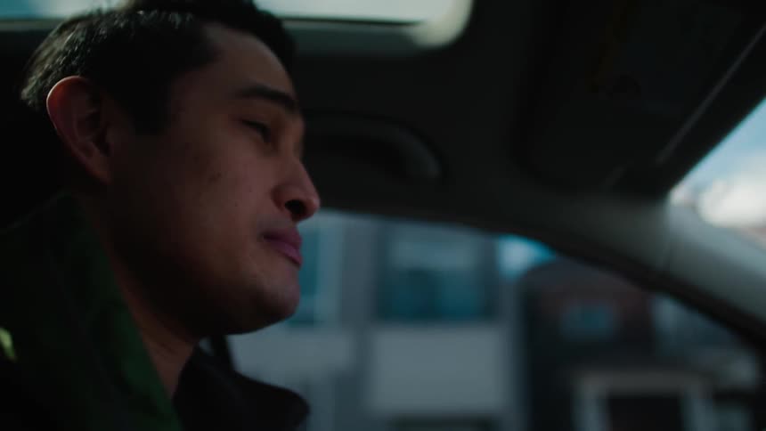 A dark-haired man drives through a city
