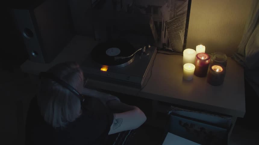 A woman is sitting in a candlelit room listening to a vinyl record