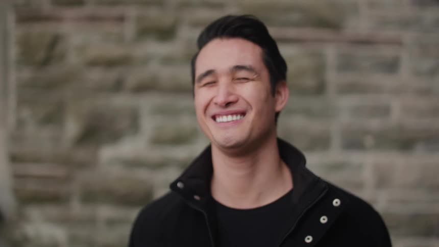 A man is smiling outside by a brick wall