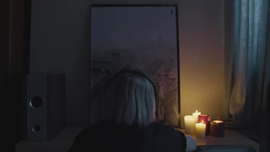 Woman sits at a desk taking her headphones off in a dark candle lit room