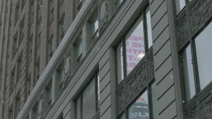 Snow slowly falls by the side of a building