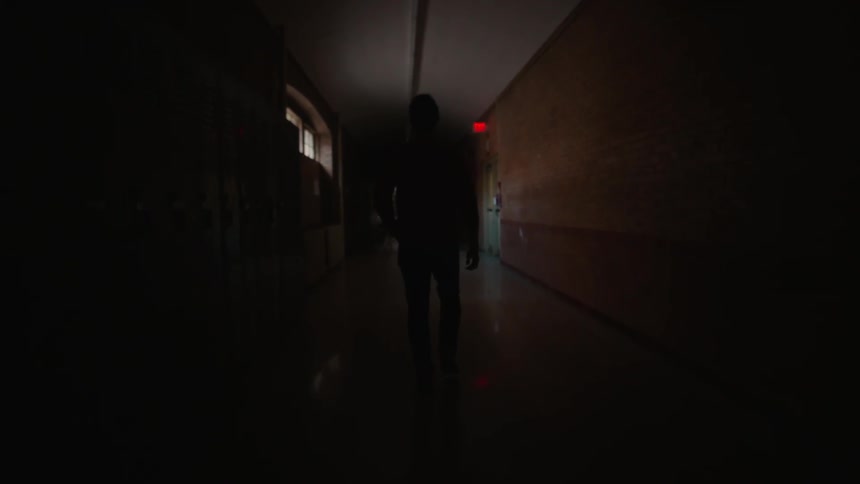 A man walks in a dark school hallway