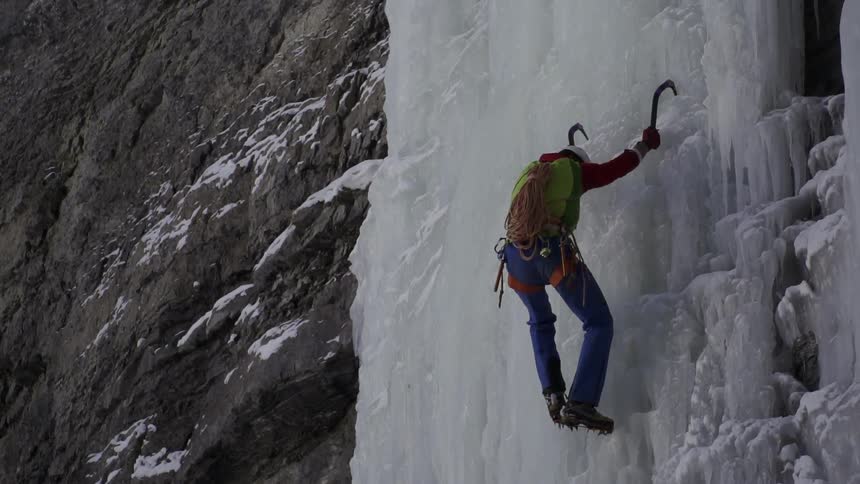 A man hanging on hooks kicks a wall of ice