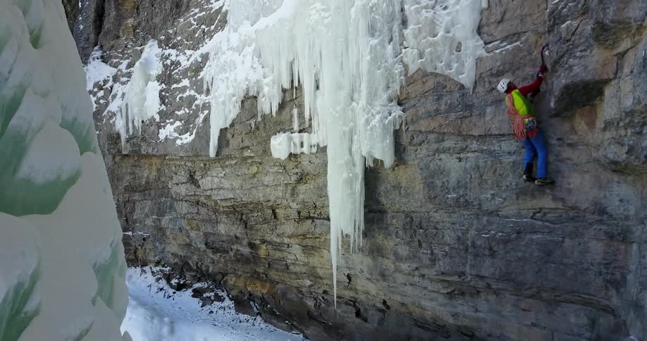 A rock climber is scaling an ice-covered rock wall
