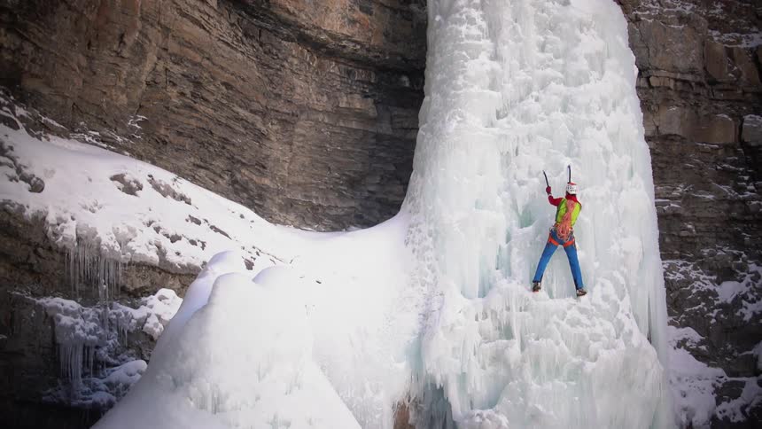 A climber is using hand axes to scale an ice wall