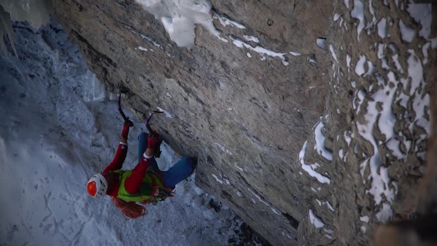 A climber uses ice axes to climb an icy cliff