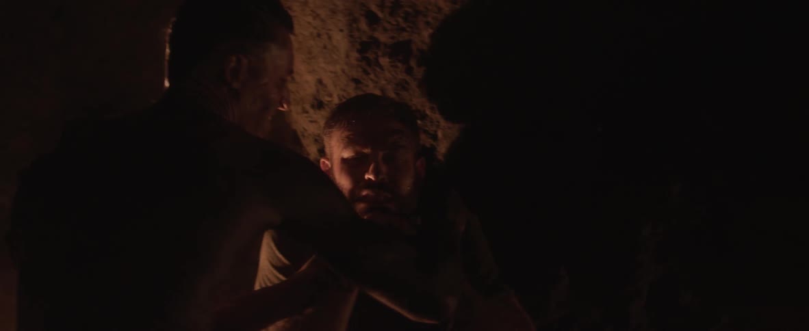 Two people fight in darkness illuminated by firelight