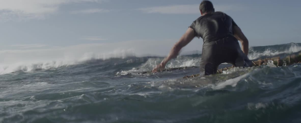 A man is trying to paddle a makeshift raft through the surf