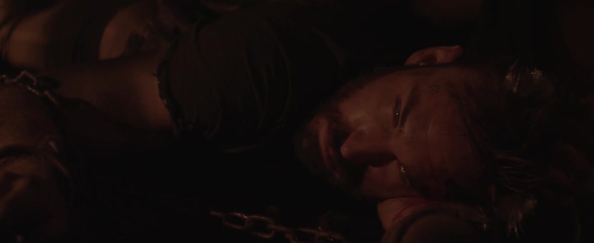 A man lays on the ground chained up