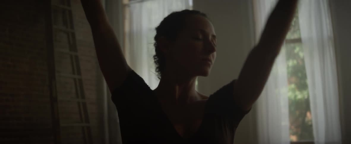 A woman dances alone in a room with a brick wall