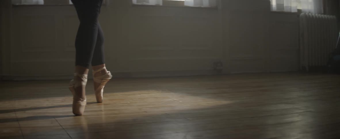 A woman begins to ballet dance on the wood floor