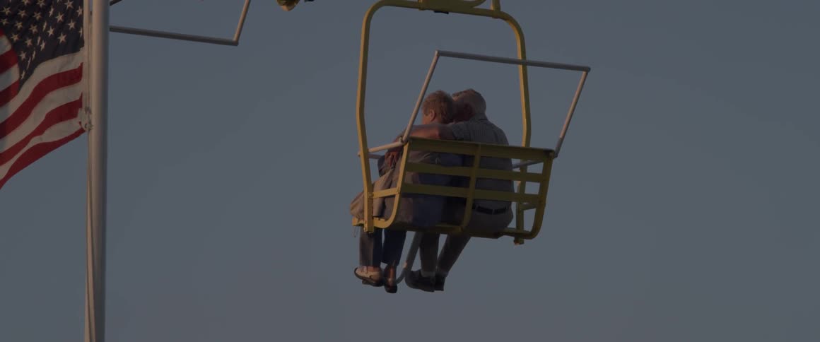 An older couple sit close together as they ride on a chair lift