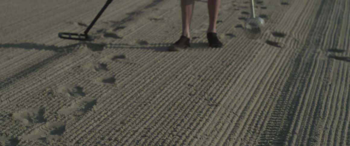 The long desert has a man using a metal detector