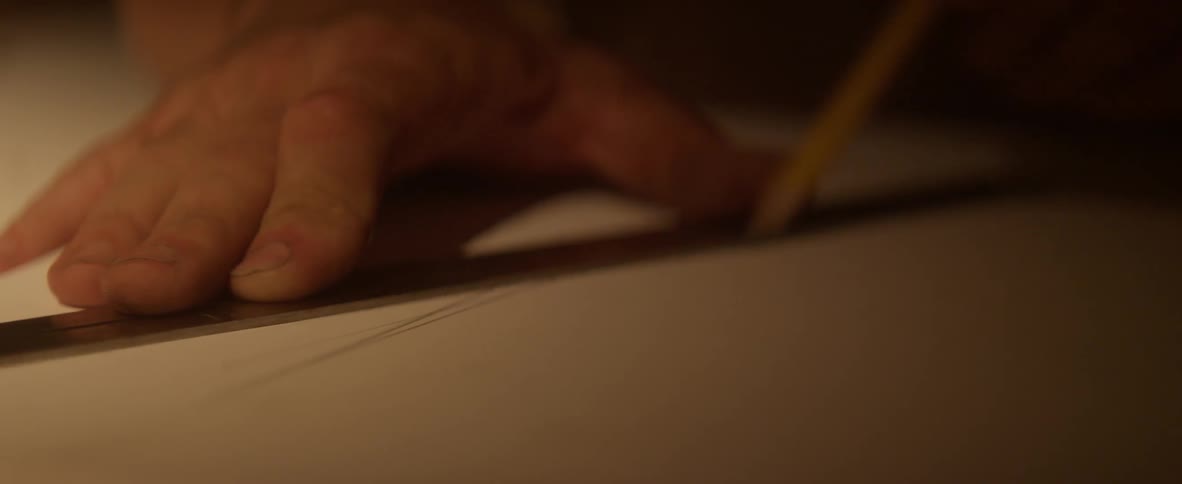A man draws on a piece of paper using a ruler