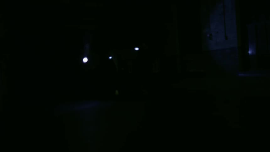 People holding flashlights jog through a dark building