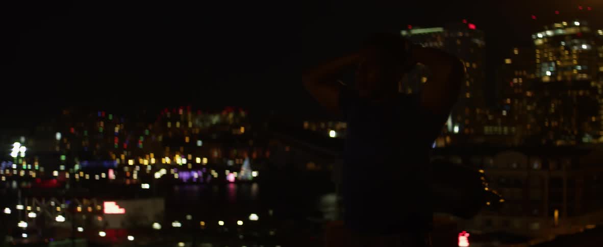 A man stands in front of city buildings at night