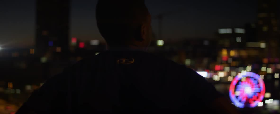A man is standing by a railing overlooking a city below at night