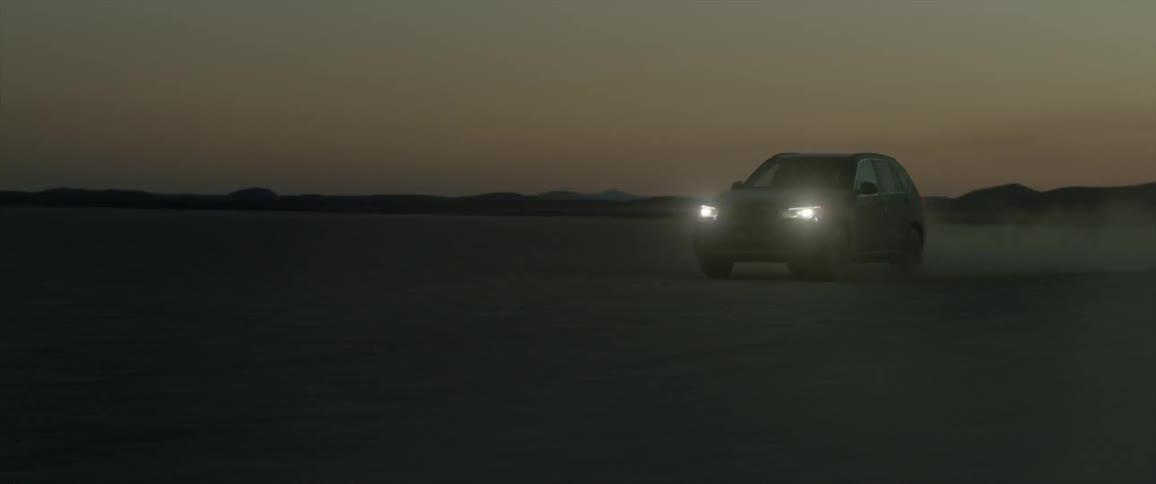 A car drives across an open field at sunset