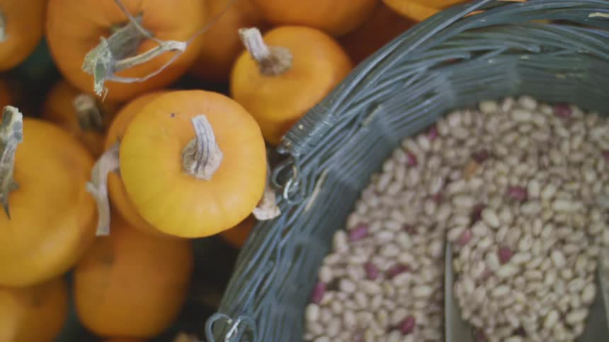 Pumpkins are stacked next to a basket of beans