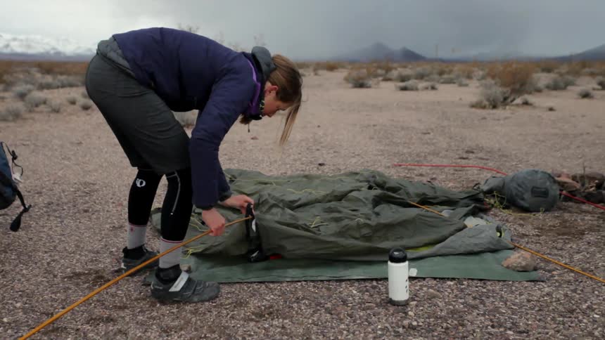 A woman is attaching a pole to a tent laying on the ground